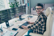 Photo of happy cheerful coder dressed eyewear writing keyboard web designing indoors workplace workstation loft
