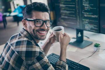 Profile photo of smart positive hacker guy arms hold fresh morning coffee toothy smile operating server open space workstation indoors