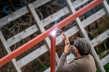 Outside the city and settlement, the master makes iron electric welding for the construction of an iron construction vineyard house (pergola) in the green area.