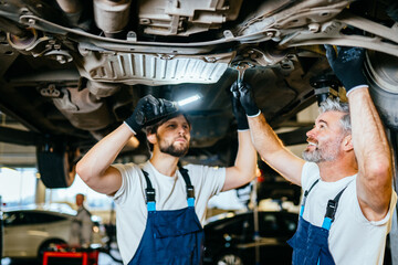 Two caucasian mechanics working about auto car engine service, technician having automotive job to maintenance or repair automobile in motor garage, business industrial auto car engin.