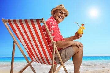 Wall Mural - Happy mature male tourist sitting at the beach with a cocktail