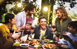 Young men and women having fun drinking out at wine diner - Food and beverage life style concept on mixed age people enjoying time together at villa patio - Warm filter with bulb string lights halo