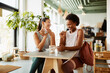 © Flamingo Images - Two diverse young female friends in sportswear laughing while sitting in a cafe and talking together over coffee after their gym workout