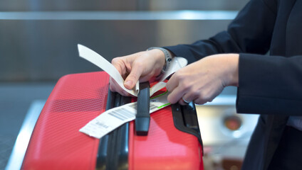 check-in employee attaches a luggage tag to suitcase of passenger - closeup of hands