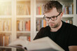 © Peter - Man holding an open book. Man is reading book. Blurred books in background.