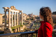 Woman in red coat looking at the Roman forum including the view of the Colosseum in the background, in Rome