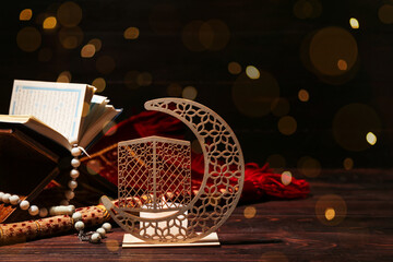 Wall Mural - Decorative crescent with burning candle, Quran book and tasbih on dark wooden table. Ramadan celebration