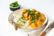 Traditional Indian dish chicken curry with basmati rice and fresh cilantro on rustic white plate on white concrete kitchen table, close up with selective focus. Indian dinner meal