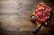© Artem Shadrin - Sliced raw beef on a plate with rosemary and seasonings in a bowl.