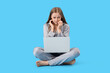 © Pixel-Shot - Young woman in pajamas with laptop biting nails on blue background