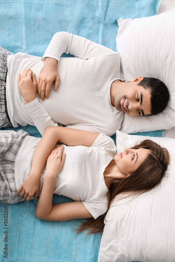 Young couple lying on electric heating pad in bedroom, top view