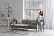 © Pixel-Shot - Young woman sitting on grey couch in living room