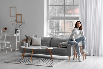 Poster - Young woman sitting on grey couch in living room