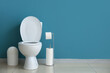 Ceramic toilet bowl, bin and paper rolls near blue wall