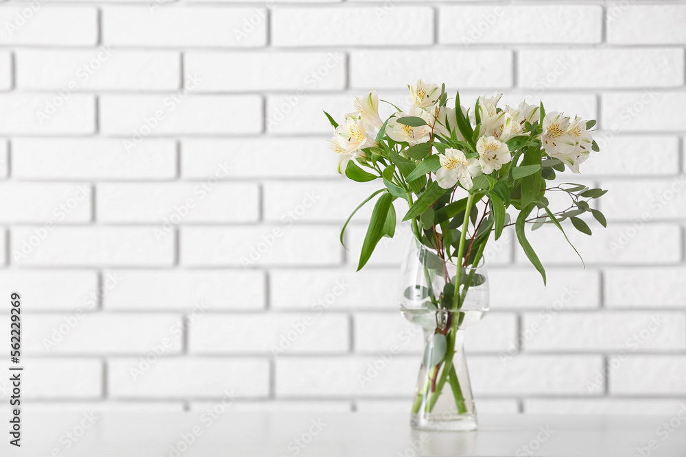 Vase with beautiful alstroemeria flowers on table near light brick wall