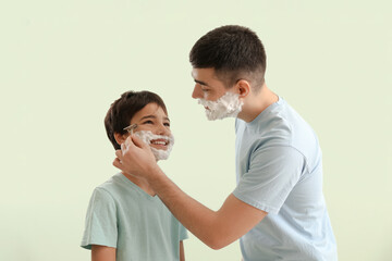 Wall Mural - Man and his little son shaving against light color background