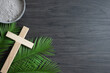 Border of small wood cross, palm leaves and bowl of ashes on a dark wood background with copy space