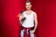 gay handsome handyman with red cordless drill machine stand isolated on red studio background and pose with joyful smile at camera and hand on pocket like a cliché pose of male calendar