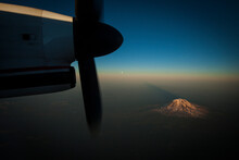 A Snow Capped Mountain Seen At Sunset Through An Airplane Window With The Propeller As A Frame.