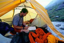 A Man Writing In A Journal In A Tent.