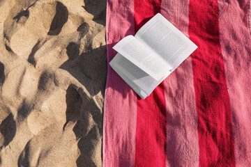 Wall Mural - Beach towel and open book on sand, flat lay. Space for text