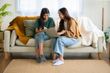 Two asian young woman happy smiling and using computer laptop on couch in living room at home