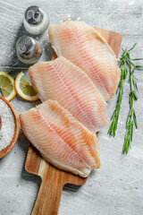 Canvas Print - Fish fillet on a wooden cutting Board with rosemary, spices and lemon slices.