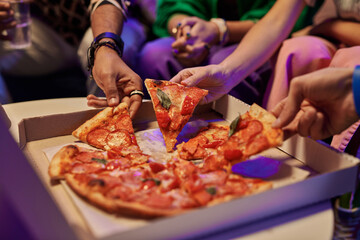 Wall Mural - Close-up of slices of appetizing pizza in square cardboard box and hands of young friends taking them and eating while enjoying home party