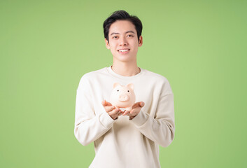 Wall Mural - Image of young Asian man holding piggy bank on background