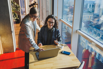 Two business women are looking for something in a laptop. Concept of business cooperation and teamwork. Young smiling women at the desk in the office. Modern successful people