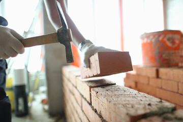 Industrial worker builds interior walls using hammer and level to place bricks into cement