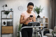 © sofiko14 - Portrait of beautiful healthy woman working out at home, running on treadmill and using phone for monitoring heart rate and time of training on background of light apartment.