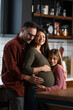 © Dorde - Affectionate young Caucasian family embracing at home while standing in the kitchen. Touching mom's pregnant belly.
