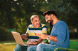 © Niks Ads - Young indian man showing bank card and laptop how to uses to his father at park
