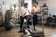 © sofiko14 - Full length portrait of focused caucasian male and african female wearing sportswear using exercise bike and treadmill. Home fitness workout sporty people training on exercise machines indoors