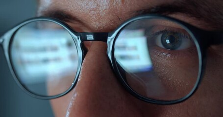 Computer Screen Reflection On Eyeglasses of man internet user surfing the net at night time. Close up man's eyes in eyeglasses scroll internet websites, monitor screen reflect searching images