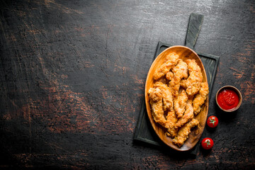 Poster - Chicken strips in a plate on a cutting Board with sauce and tomatoes.