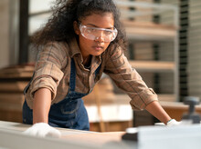 Portrait, Female Multiracial Carpenter Working In Woodshop Small Business. Afro Woman With Goggles Standing In DIY Carpentry Workshop With Confidence. Empowerment Joiner Women In Woodworking Industry