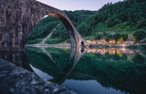 Fototapeta Koty - Il ponte del Diavolo o ponte della Maddalena a Borgo a Mozzano, in Toscana. Magica l'atmosfera con lo specchio d'acqua al crepuscolo.