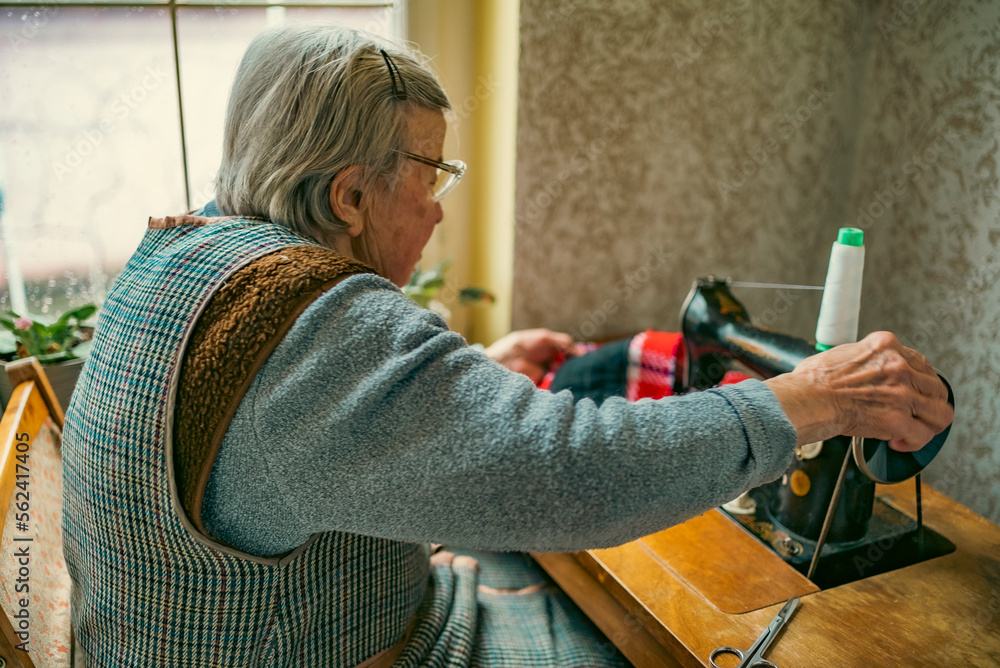 Foto Senior woman in spectacles use sewing machine. wrinkled hands of ...
