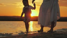 Happy Family, Mom Walks On Beach With Child Barefoot On Water In Summer, Holding Hands, Beautiful Sunset. Mother And Daughter Are Relaxing On Beach. Mom, Child Play Outdoors. Happy Family, Kid Travel