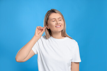 Poster - Young woman cleaning ear with cotton swab on light blue background