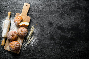 Poster - Fresh buns on a wooden cutting Board with a rolling pin and spikelets.