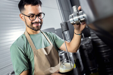 Male brewer working in craft brewery examining quality of the beer.