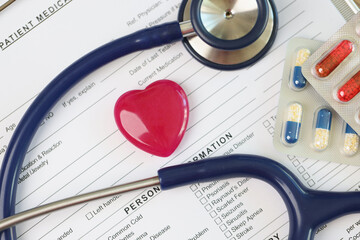 Wall Mural - Red heart with stethoscope and packs of pills on blank medical examination form.