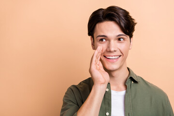 Canvas Print - Portrait of satisfied pleasant man with brunet haircut dressed khaki shirt hand mouth look empty space isolated on beige color background