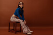 Fashionable confident woman wearing trendy brown rectangular sunglasses, stylish blue turtleneck, flared trousers with zebra print, boots. Full-length studio portrait. Copy, empty space for text