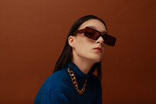 Fashionable confident woman wearing trendy brown rectangular sunglasses, chunky chain, stylish blue turtleneck. Close up studio portrait. Copy, empty space for text