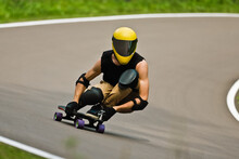 A Man In A Yellow Helmet And Leather Suit, In A Rack At High Speed, Rides On A Long Longboard For Downhill On Asphalt