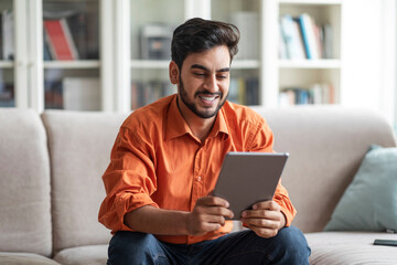 Wall Mural - Happy middle eastern guy using digital tablet at home